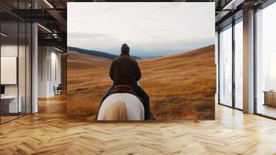 Rider on horseback explores scenic golden hills at dusk with a panoramic view in the background Wall mural