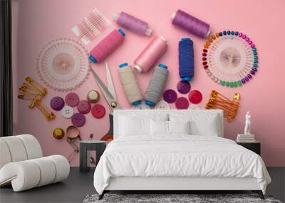 Sewing accessories including thread spools and pins on pink background Wall mural