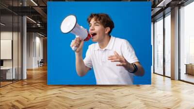 Teen boy making loud announcement against blue background. Wall mural