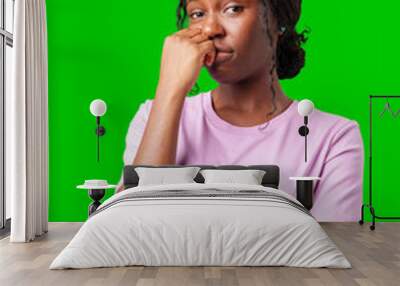 Thoughtful woman pondering in front of a bright green background during a casual moment Wall mural