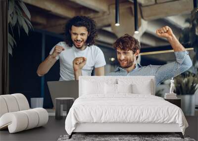 Two excited overjoyed young businessmen looking at laptop screen happy to win or recieved good news Wall mural