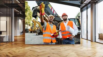 Two men engineers discussing their work standing against construction machines Wall mural