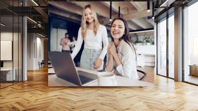 Two young happy businesswomen celebrating project success in office Wall mural