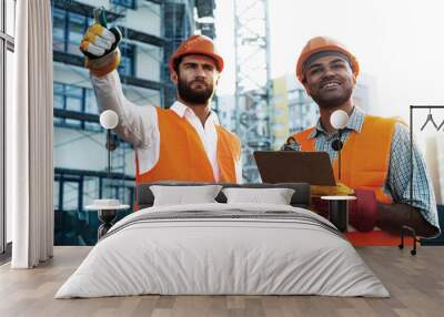 Two young male engineers in uniform and hardhats working at construction site Wall mural