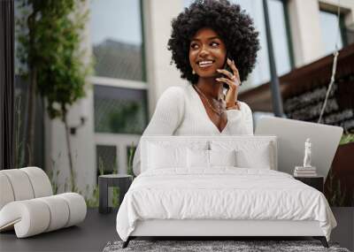 Young african american businesswoman working using laptop sitting on the bench in the city Wall mural