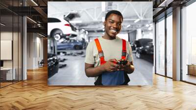 Young African mechanic man wearing uniform using mobile phone in a car service Wall mural