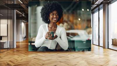 Young afro woman taking break and drinking coffee in cafe Wall mural