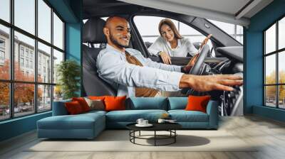 Young attractive woman salesperson in car showroom showing a car to her male client Wall mural