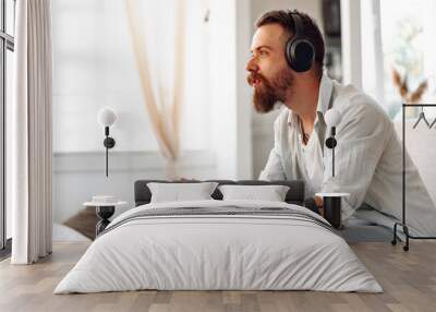 Young bearded man playing video games while sitting on the couch at home Wall mural