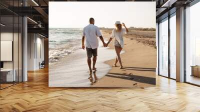 Young beautiful couple walking on beach near sea Wall mural