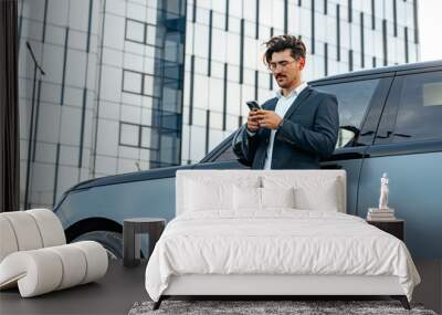 Young businessman standing near luxury car and using smartphone Wall mural