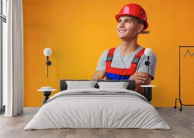 Young construction worker in helmet and uniform posing on yellow background in studio Wall mural