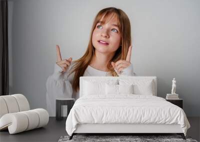 Young girl in a white sweater pointing against a plain background Wall mural