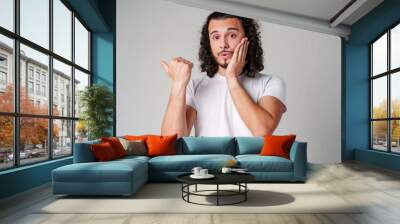 Young man in a white t-shirt and jeans pointing confidently while smiling in a studio setting Wall mural