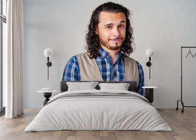 Young man in plaid shirt and vest poses confidently against a neutral background Wall mural