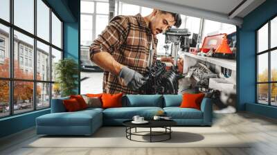 Young man mechanic repairing car parts on worktable in car service shop Wall mural