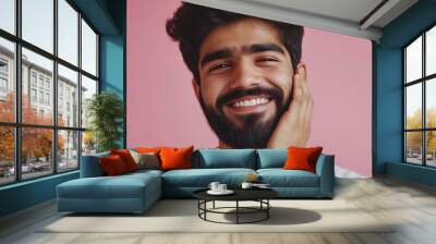 Young man smiling with a beard while standing against a pink background, showcasing joy and confidence in a casual setting Wall mural