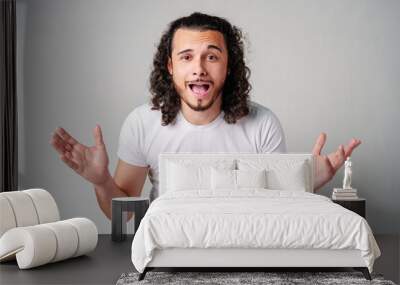 Young man with curly hair expresses surprise in a light-colored setting Wall mural