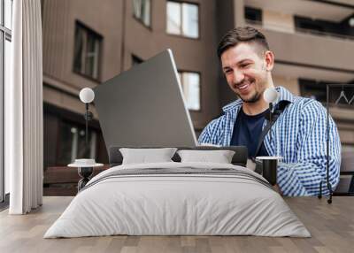 Young man working on a laptop while seated on a bench outside Wall mural