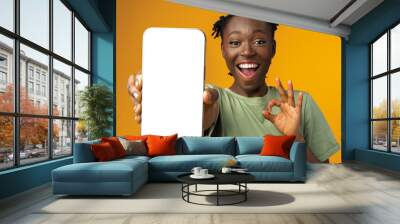 Young smiling african american woman showing smartphone with blank screen against yellow background Wall mural