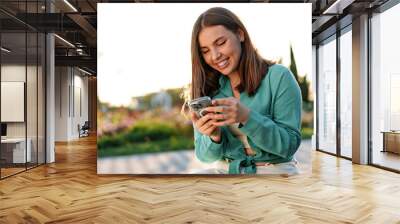 Young woman using a smartphone in the park Wall mural