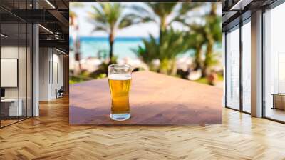 Cooled glass of beer with condensation drops on the blue wooden table. Blurred sea is at the background. Wall mural