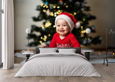 adorable little baby boy in a red christmas outfit sitting on a soft fake fur in front of a christmas tree Wall mural