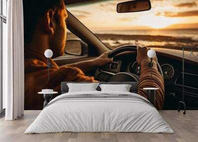 A man is seen driving a car on the beach at sunset. This image can be used to depict a leisurely beach drive or the freedom of a road trip by the coast. Wall mural