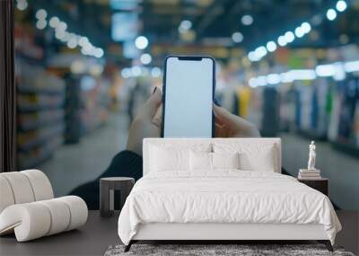 A person examining a product in a store while holding their smartphone Wall mural