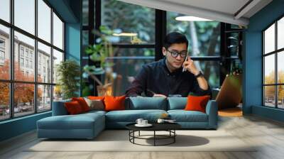 A person sitting at a table with a laptop and a cell phone, focused on work Wall mural