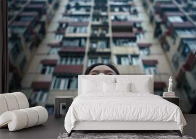 A person wearing a face mask in front of a tall building. Suitable for illustrating urban lifestyle during pandemic Wall mural