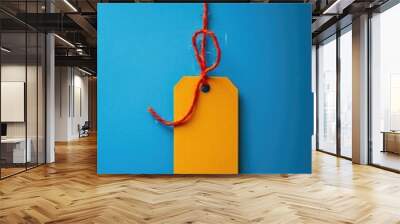 A single yellow tag hanging from a string against a blue background, great for use as a placeholder or icon Wall mural