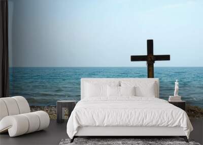 A wooden cross sits atop a sandy beach, surrounded by calm waters Wall mural