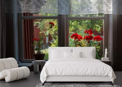 Two red geraniums in an old window with white lace curtains, with a nice garden outside Wall mural