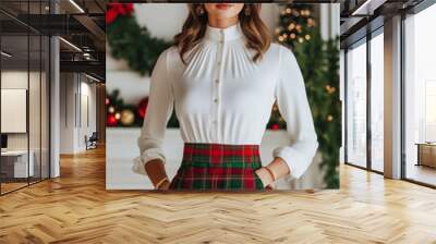 Stylish holiday ensemble featuring a woman in a red and green tartan skirt paired with a white blouse and gold accessories cozy Christmas setting with stockings and wreaths  Wall mural