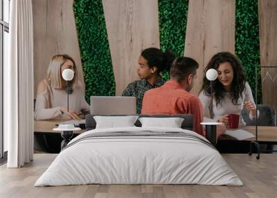 Diverse group of smiling young designer working together over a laptop during a meeting in the boardroom of a modern office Wall mural