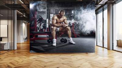 bodybuilder athletic guy relaxing after workout in gym Wall mural