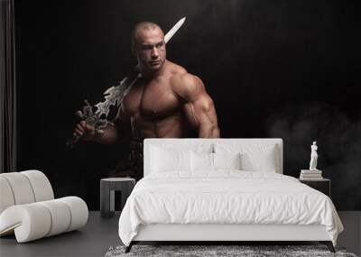 Ferocious muscular ancient warrior barbarian with fantasy sword on black background Wall mural