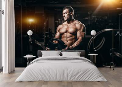 Muscular man bodybuilder training in gym and posing. Fit muscle guy workout with weights and barbell Wall mural