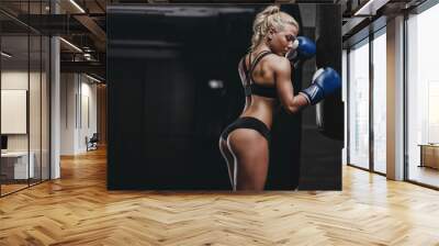 sexy young athletics muscled blonde girl relax after training with boxing gloves and lean to punching bag. Fitness muscled woman in sport clothing posing Wall mural