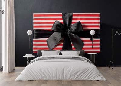  Gift box wrapped in red striped paper with a black bow, placed against a black background f_1(322) Wall mural