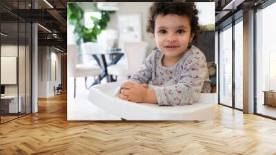 Cute two year old baby girl sitting on a high chair in a home setting Wall mural