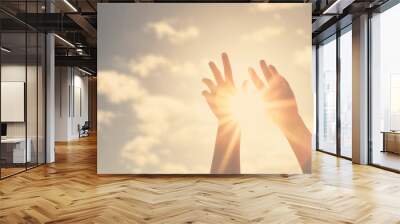 Woman hands reaches for the sky and closes the sun, the sun's rays pass through the hand Wall mural