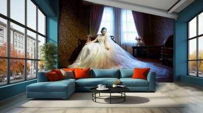 A beautiful young bride in a white wedding dress is sitting on the sofa. Wall mural