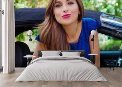 Close up of beautiful woman wearing a blue dress and posing inside of a luxury black car on a roadtrip. the car standing on the sidelines, in a blurred nature background Wall mural