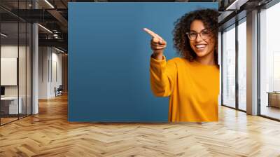 Beautiful young black woman pointing up to copy space and smiling, happy, Pretty girl act like satisfied at the product, use for advertising , isolated on blue background Wall mural