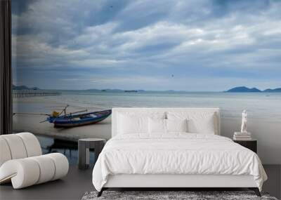 tranquil beach scene with a solitary wooden boat on white sand, a long pier, and distant mountains u Wall mural