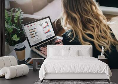 Rear view. Young businesswoman is sitting at table, working on laptop with graphs, charts, diagrams, schedules on screen Wall mural