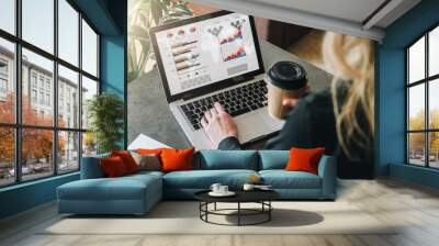 Rear view.Young businesswoman is standing near table,working on laptop with graphs, charts,diagrams, schedules on screen Wall mural