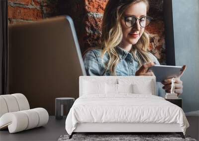 Young woman sits in cafe on windowsill and uses smartphone. Hipster girl checking e-mail, chatting, blogging, working. Wall mural